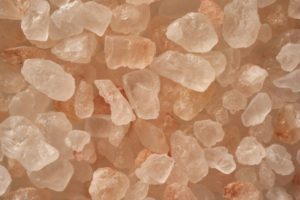 Close-up van verschillende onregelmatig gevormde roze Himalaya-zoutkristallen, variërend in kleur van wit tot lichtroze en oranje, die samenkomen tegen een neutrale achtergrond.