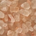 Close-up van verschillende onregelmatig gevormde roze Himalaya-zoutkristallen, variërend in kleur van wit tot lichtroze en oranje, die samenkomen tegen een neutrale achtergrond.