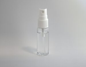 Een klein, doorzichtig plastic spuitflesje met een witte spuitmond en dop, gevuld met een transparante vloeistof, rechtopstaand tegen een effen, lichtgrijze achtergrond.